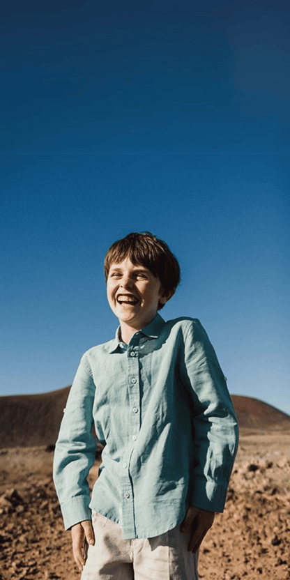 Niño sonriendo al aire libre vistiendo una camisa de lino verde y pantalón beige de Boboli, ideal para ocasiones especiales y eventos formales.