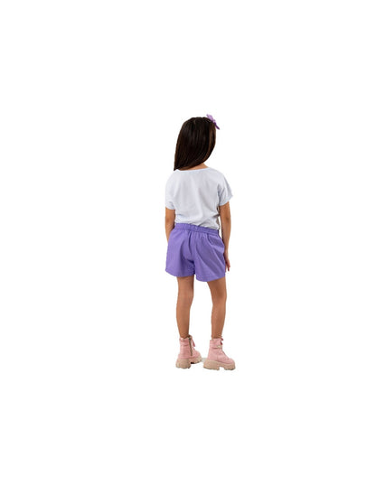 Vista trasera de una niña con outfit infantil compuesto por una blusa blanca, shorts morados con cintura elástica y botines rosas, creando un look cómodo y moderno para cualquier ocasión.
