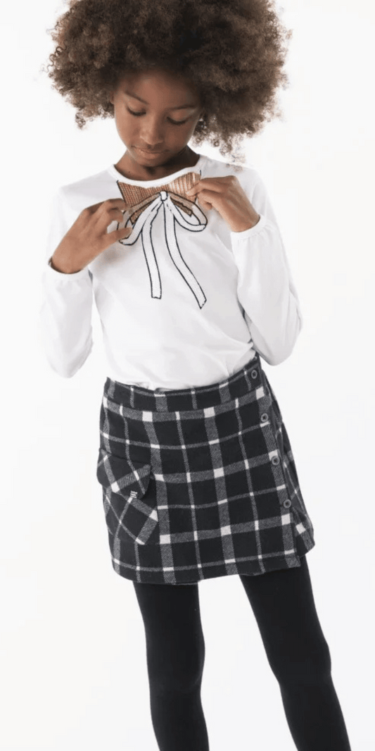 Niña usando conjunto Boboli con falda de cuadros y playera blanca con moño de lentejuelas doradas