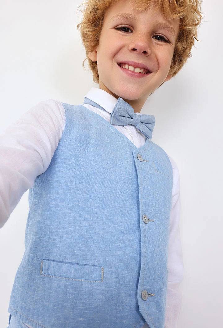 Primer plano de niño sonriendo con chaleco de lino azul y moño, conjunto formal de Boboli.
