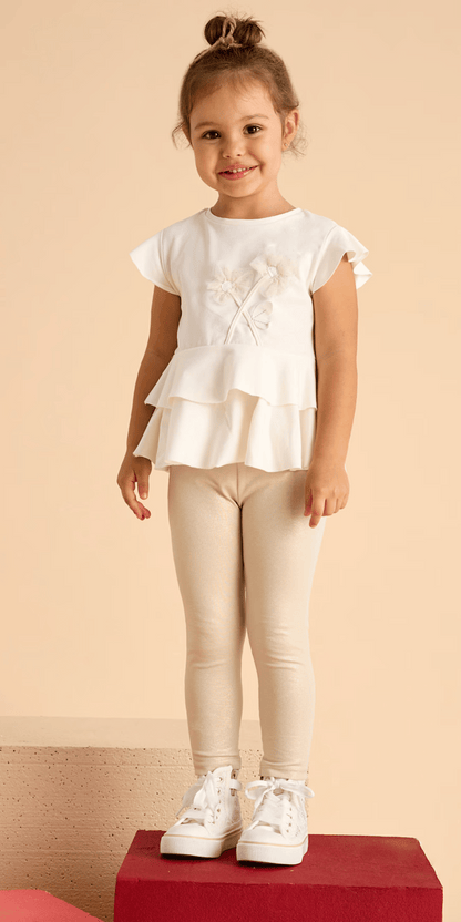 Niña sonriente usando un conjunto de playera con flores y leggings brillosos en tono beige de la marca Mayoral.