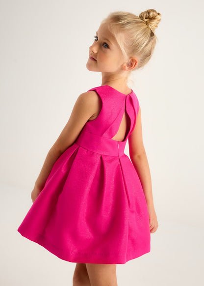 Niña usando un vestido magenta fiusha de Mayoral visto desde la espalda, con diseño elegante y detalles plisados.