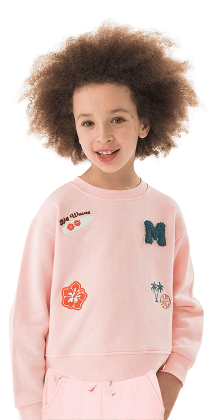 Niña usando conjunto de sudadera y pants rosas con parches bordados de estilo tropical.