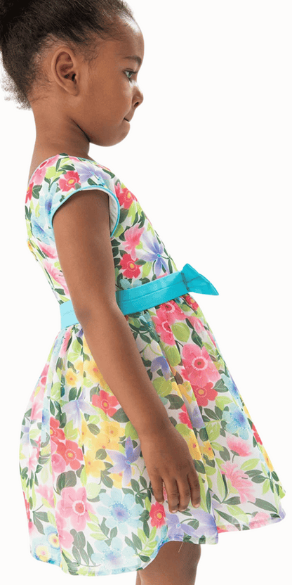 Niña modelando un vestido de gasa con estampado floral y cinturón azul, ideal para ocasiones especiales.