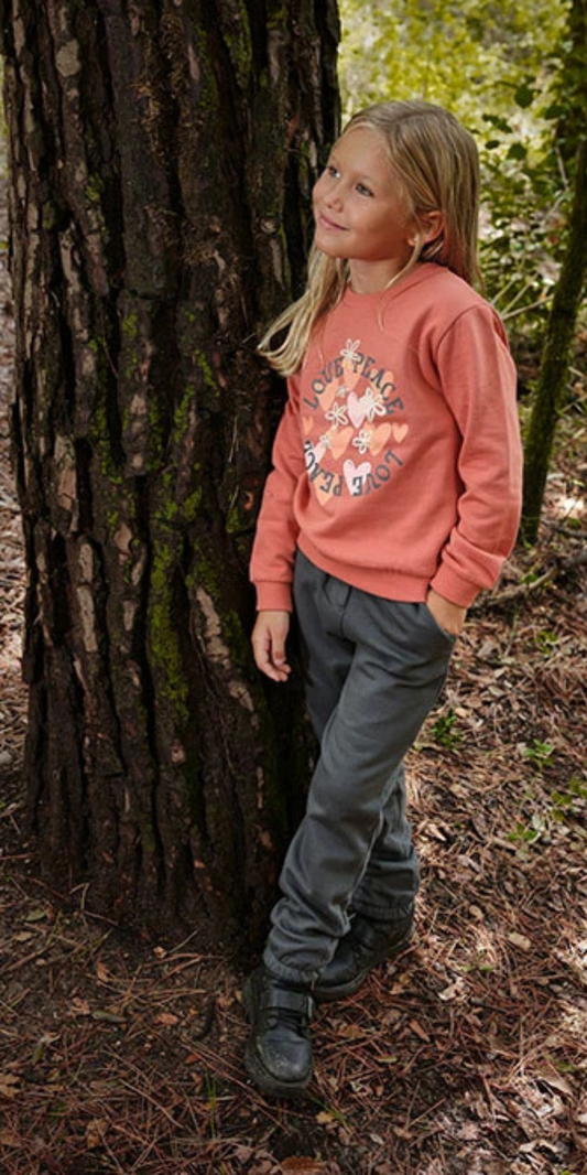 Niña apoyada en un árbol, usando un conjunto de sudadera color teja y pants oscuros con estampado "Love & Peace", marca Boboli.