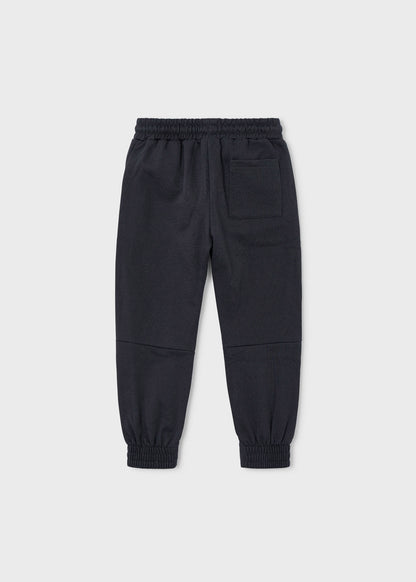 Vista trasera de un pantalón jogger de felpa color gris oscuro para niño, con paneles en las rodillas.