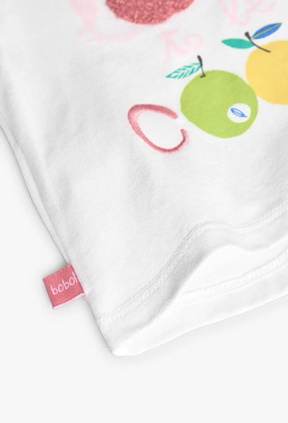 Detalle del estampado en una playera blanca para bebé, con manzana y peras en colores vibrantes y textura bordada.