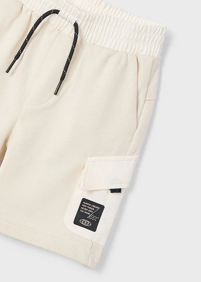 Detalle de shorts beige Mayoral con bolsillo lateral y etiqueta con mensaje de diseño urbano.