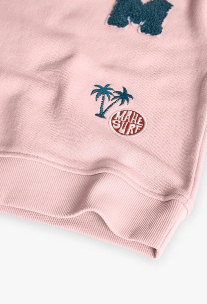 Detalle de parches bordados de palmeras y texto “Mahe Surf” en sudadera rosa.