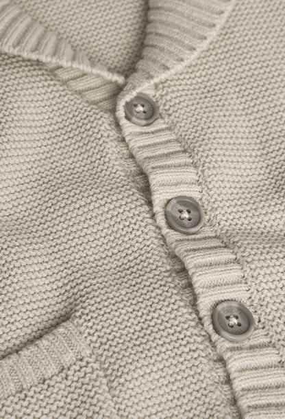 Primer plano de un suéter beige tejido con botones, resaltando la textura y los detalles de su confección.