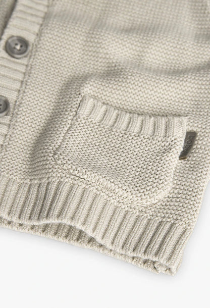 Detalle del bolsillo frontal de un suéter beige tejido para niños, mostrando textura y acabado.