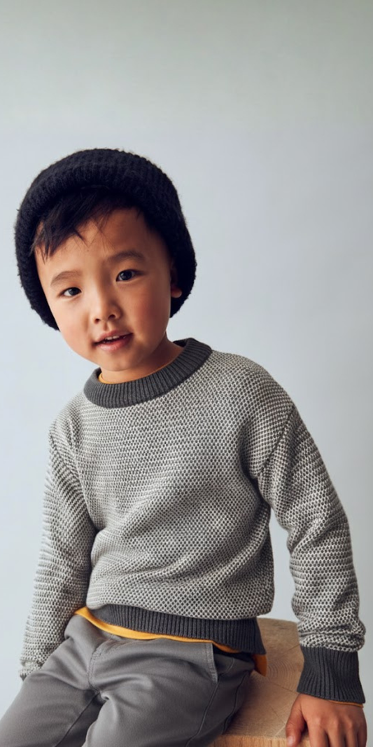 Niño posando con un suéter de punto bicolor, gorro negro y pantalones grises, marca Mayoral.