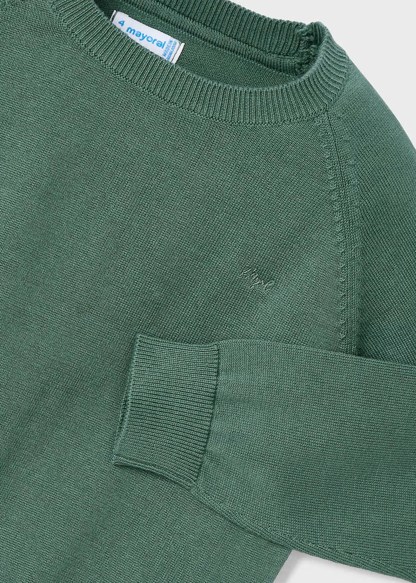 Detalle del cuello, hombro y puño de un suéter verde de tricot Mayoral, mostrando la textura del tejido y el logotipo bordado en el pecho.