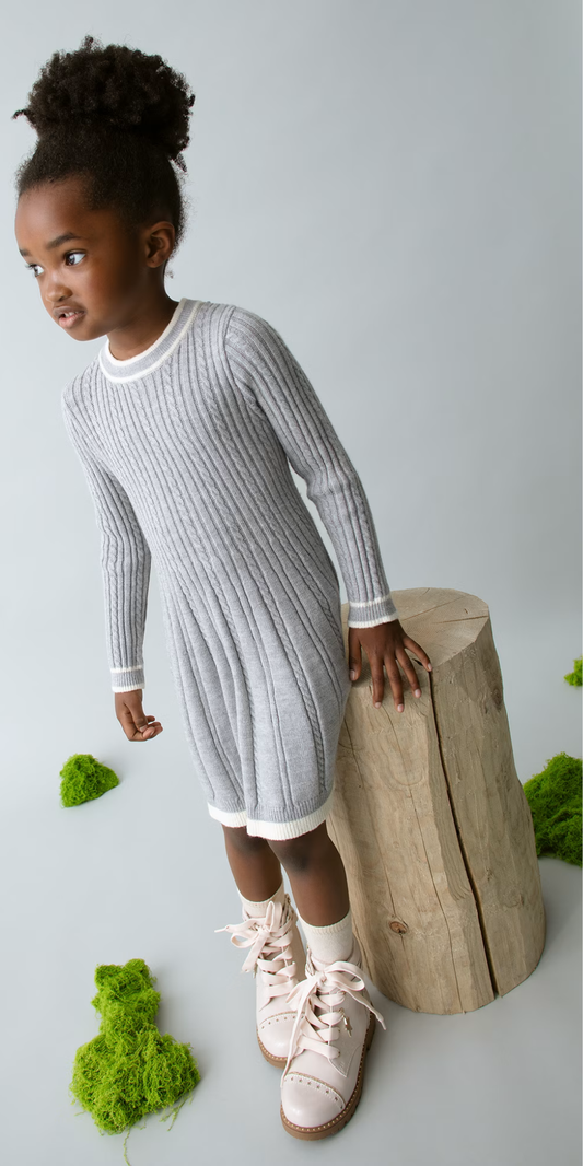 Niña posando junto a un tronco con un vestido de punto gris de manga larga y detalles a contraste, marca Mayoral.