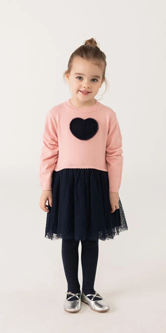 Niña sonriendo con un vestido de punto rosa y falda de tul azul marino, con un aplique de corazón en el pecho, marca Boboli. 